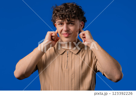 Annoyed man with shut ears on blue. Guy block annoying sounds, loud music, noise Annoyed man with shut ears on blue. Guy block annoying sounds, loud music, noise 123392226