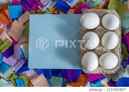 Easter eggs with a blank card surrounded by colorful festive paper pieces Easter eggs with a blank card surrounded by colorful festive paper pieces 123392907