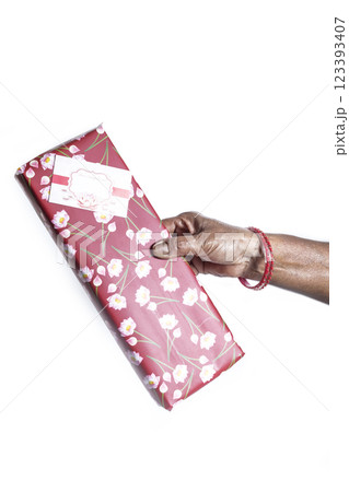 Hand holding a gift wrapped in red paper with a floral design printed on it, on a white background. Hand holding a gift wrapped in red paper with a floral design printed on it, on a white background. 123393407