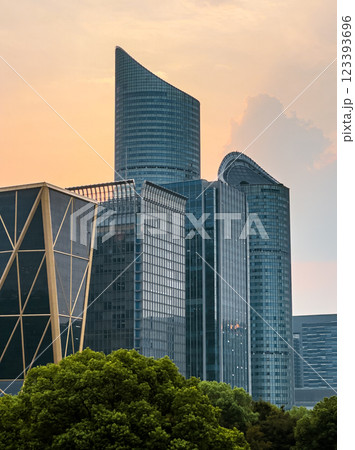 Modern skyscrapers illuminated by sunset in an urban setting near a lush green park 123393696