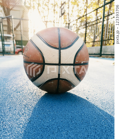 Basketball resting on a blue court during golden hour with sunlight illuminating the background 123393706