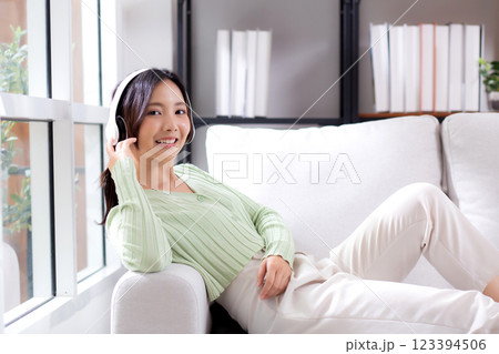 Happy young asian woman wearing headphones listening music while sitting on sofa with fun. Happy young asian woman wearing headphones listening music while sitting on sofa with fun. 123394506