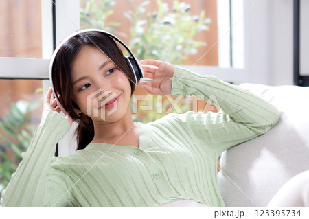 Happy young asian woman wearing headphones listening music while sitting on sofa with fun. Happy young asian woman wearing headphones listening music while sitting on sofa with fun. 123395734