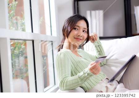 Young asian woman sitting on sofa using tablet computer shopping online with credit card. 123395742