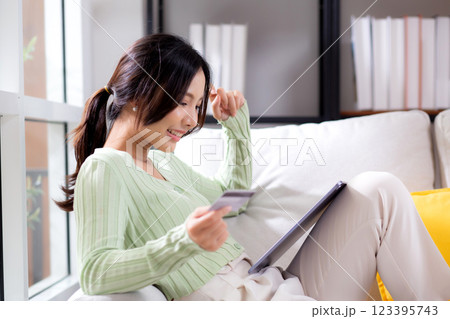 Young asian woman sitting on sofa using tablet computer shopping online with credit card. 123395743