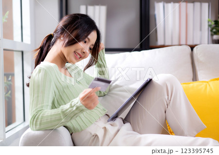 Young asian woman sitting on sofa using tablet computer shopping online with credit card. 123395745