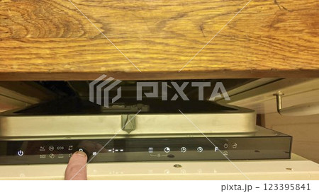 A male finger on the control panel of the dishwasher. Changing cycles on the dishwasher. Illuminated buttons on the dishwasher's digital display. Closing the door of the built-in dishwasher 123395841