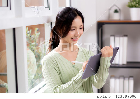 Young asian woman using tablet writing with inspiration and comfortable by window. 123395906