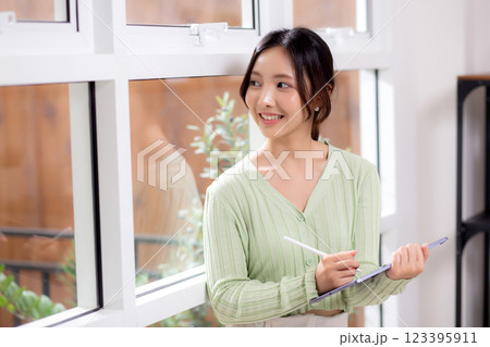 Young asian woman using tablet writing with inspiration and comfortable by window. 123395911