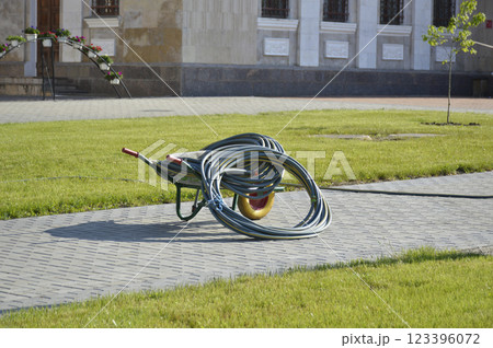 wheelbarrow and hose for watering on an alley in the park wheelbarrow and hose for watering on an alley in the park 123396072