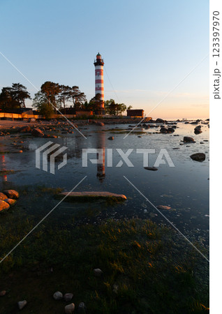 Dramatic sunset at a lighthouse on the coast. Lighthouse with white and red stripes among trees Dramatic sunset at a lighthouse on the coast. Lighthouse with white and red stripes among trees 123397970