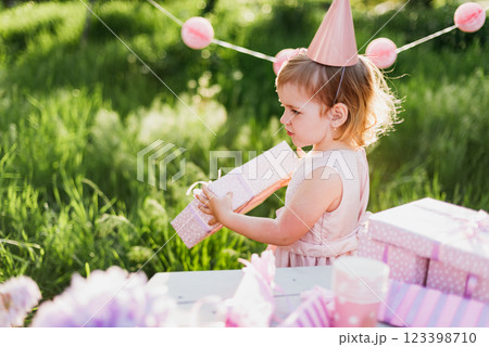 Happy birthday little girl with gift box in beautiful garden. child eat happy birthday rose cupcake. colorful pastel decoration outdoor. 4 years old kid celebrating enjoying party on summer day. 123398710