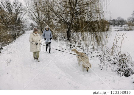 Two women walking a Golden Retriever on a snowy path, enjoying winter nature together. Two women walking a Golden Retriever on a snowy path, enjoying winter nature together. 123398939