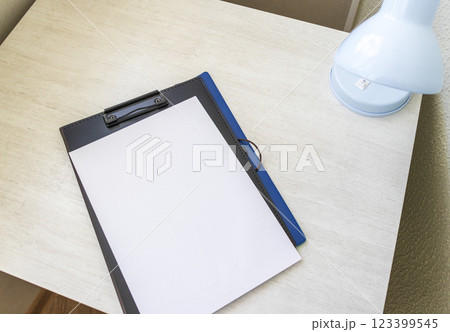 Shot of the plastic folder on the office desk with paper clip holder on the top and other office items. A4 size paper mock up. Shot of the plastic folder on the office desk with paper clip holder on the top and other office items. A4 size paper mock up. 123399545