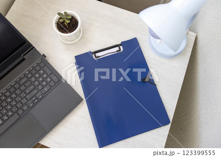 Shot of the plastic folder on the office desk with paper clip holder on the top and other office items. A4 size paper mock up. Shot of the plastic folder on the office desk with paper clip holder on the top and other office items. A4 size paper mock up. 123399555