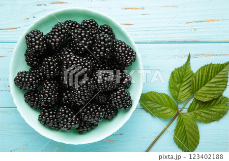 Ripe blackberries with leaves in mint bowl on blue wooden background. 123402188