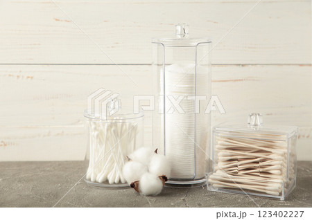 Cotton pads and cotton sticks in containers with cotton flower on grey background. 123402227