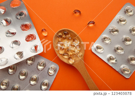 Vitamin D yellow pills on wood spoon on orange background. Medicine tablets of vitamin d on table. Vitamin D yellow pills on wood spoon on orange background. Medicine tablets of vitamin d on table. 123403078