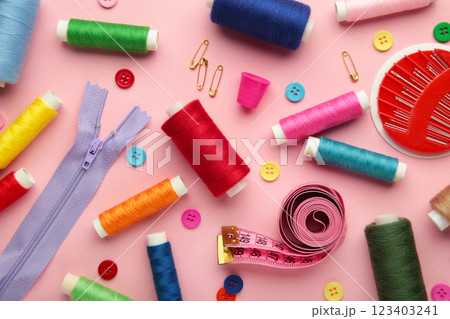 Sewing supplies on pink background: sewing thread, scissors, a large spool of thread, pieces of cloth, needles,centimeter, buttons Sewing supplies on pink background: sewing thread, scissors, a large spool of thread, pieces of cloth, needles,centimeter, buttons 123403241