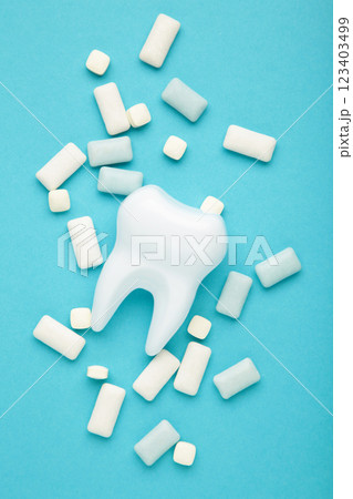 White healthy tooth model and heap of chewing gums on blue background. Concept of oral dental hygiene Vertical photo 123403499