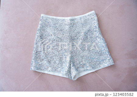 A pair of sequined silver shorts displayed on a soft pink surface. 123403582