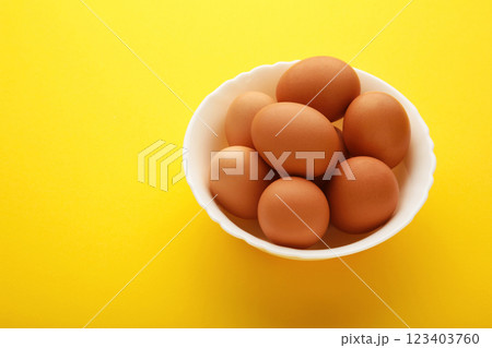 Top view of raw brown eggs on plate on yellow background. Eggs are a common ingredient in cooking. Top view of raw brown eggs on plate on yellow background. Eggs are a common ingredient in cooking. 123403760