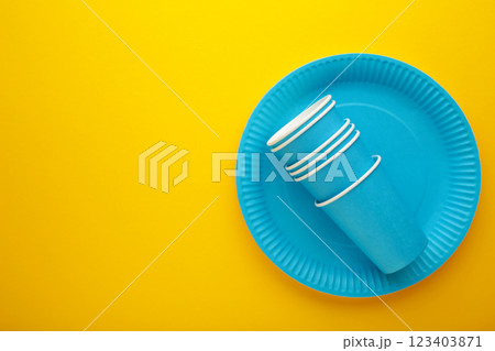 Eco-friendly disposable utensils made of craft paper on yellow background. Blue plates and paper cups Eco-friendly disposable utensils made of craft paper on yellow background. Blue plates and paper cups 123403871