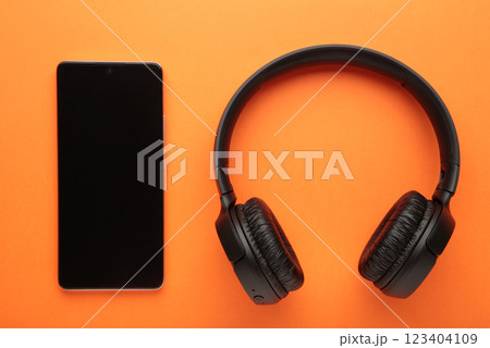 Black smartphone and wireless headphones on a orange background. 123404109