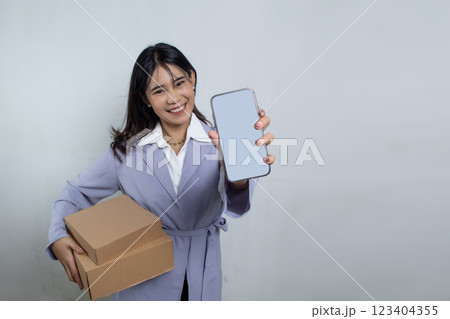 Beautiful Asian woman with long hair receiving cardboard box package using smartphone in navy blue suit on white background, advertising woman shopping online 123404355