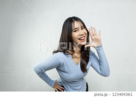 happy and hysterical young asian girl with her body bent over with both hands covering her mouth as if to invite something, the woman is wearing a blue casual top, white background happy and hysterical young asian girl with her body bent over with both hands covering her mouth as if to invite something, the woman is wearing a blue casual top, white background 123404361