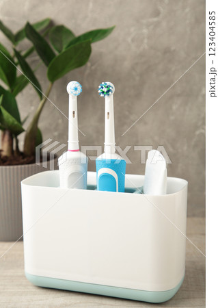 Holder with modern electric toothbrushes and plant on blue background 123404585