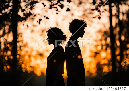 Two people stand back-to-back in silhouette against a vibrant sunset backdrop, expressing concepts of relationship, introspection, or conflict. Symbolizes Valentine's Day. 123405237