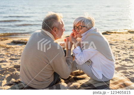 Senior mature couple sitting on beach holding hands enjoying outdoor recreation. Old husband wife touching hands with tenderness love. Grandmother grandfather together. Family moment of love Senior mature couple sitting on beach holding hands enjoying outdoor recreation. Old husband wife touching hands with tenderness love. Grandmother grandfather together. Family moment of love 123405815