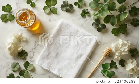 A blank white towel laying with a golden honey jar and clovers lying around it. 123406288