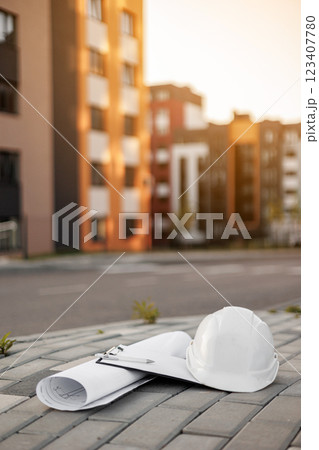 View on blueprint, protective white hard hat and clipboard folder with pen on multi-apartment residential complex background. Safety construction equipments of architect, engineer, inspector or worker View on blueprint, protective white hard hat and clipboard folder with pen on multi-apartment residential complex background. Safety construction equipments of architect, engineer, inspector or worker 123407780