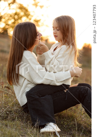 Family day, mother's day. Happy smiling young mom and adorable child daughter soft hugging, kissing and spending time together at autumn on sunset. Idyllic family having fun outdoors on fall holiday. 123407793