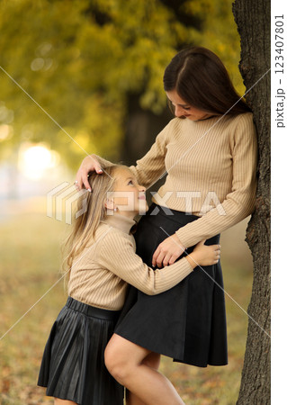 Family day. Young mom and little daughter having fun and enjoy relaxing outdoors in autumn park. Adorable child girl tightly hugs and kiss her mother. Maternal care and love for kid. Mothers day 123407801