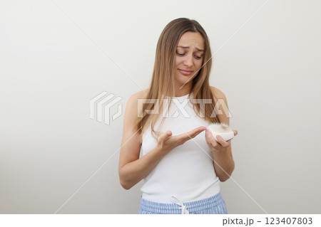 Frustrated young woman with hair loss problem holds hair brush and shows on bunch of fallen hair after combing. Alopecia, endocrine disorder, hormonal imbalance, postpartum period, stress concept 123407803