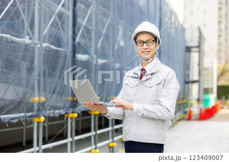 ノートパソコンを持つ作業着の男性 ノートパソコンを持つ作業着の男性 123409007