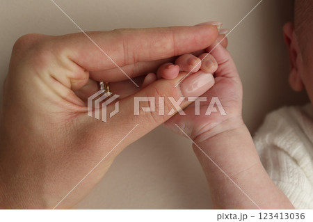 Close-up little hand of child and palm of mother and father. The newborn baby has a firm grip on the parent's finger after birth. A newborn holds on to mom's, dad's finger.  123413036