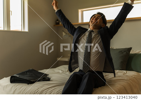 ベッドに座る疲れたスーツ姿の若いビジネスマン(飲み過ぎ・二日酔い・朝帰り・酔っ払い) ベッドに座る疲れたスーツ姿の若いビジネスマン(飲み過ぎ・二日酔い・朝帰り・酔っ払い) 123413040