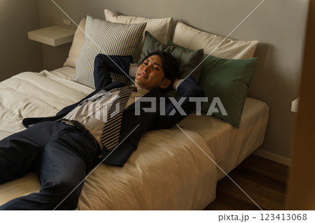 帰宅後スーツのままベッドで横になる若いアジア人男性ビジネスマン 123413068