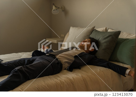 帰宅後スーツのままベッドで横になる若いアジア人男性ビジネスマン 帰宅後スーツのままベッドで横になる若いアジア人男性ビジネスマン 123413070