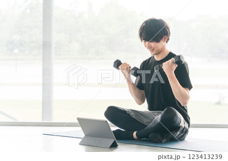 動画を見ながらダンベルで筋トレ・ワークアウト・ウエイトトレーニング・ボディメイク・筋肉を鍛える男性 123413239