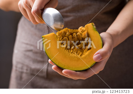 Hand holding spoon and removing seeds from pumpkin, Homemade cooking 123413723