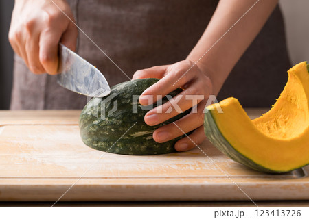 Hand holding kitchen knife and cutting green pumpkin on wooden board, Homemade cooking 123413726