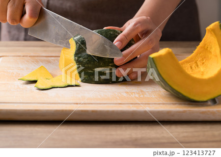 Hand holding kitchen knife and cutting green pumpkin on wooden board, Homemade cooking 123413727