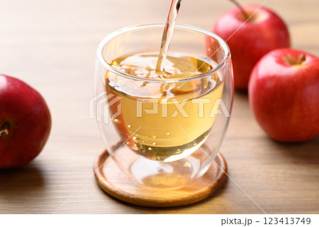 Apple cider pouring into glass with apple fruit on wooden background Apple cider pouring into glass with apple fruit on wooden background 123413749