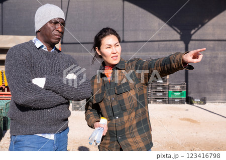 Asian female farmer giving instructions to worker outdoors at farm 123416798