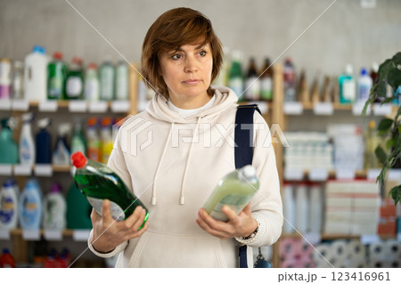 Female shopper selects dishwashing liquid n the household goods section of supermarket Female shopper selects dishwashing liquid n the household goods section of supermarket 123416961